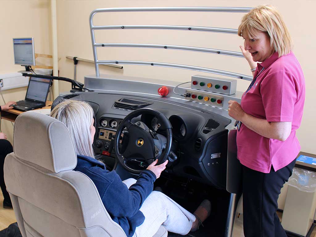 A woman conducting a driving assessment using a mock up of a car driving console.