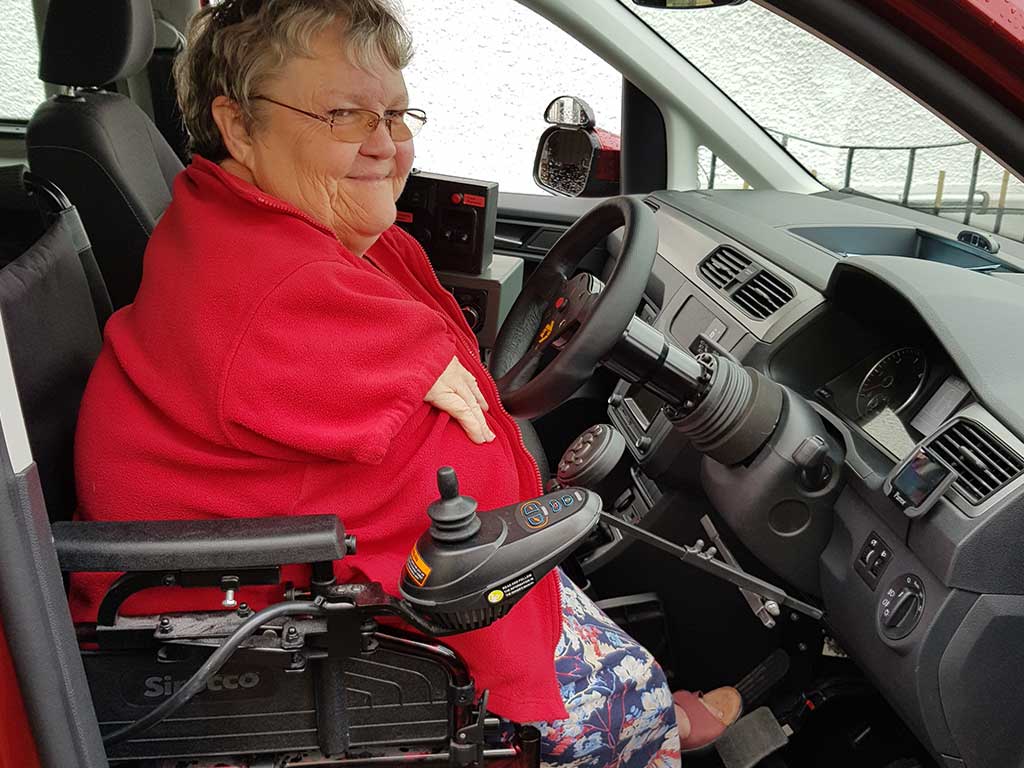 A woman in a red jumper trying out the assistive technology in her car.