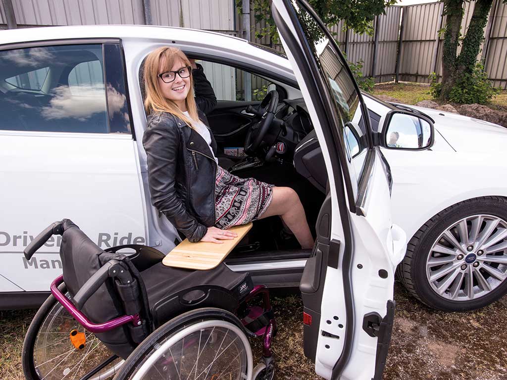 A young woman transitioning from her wheelchair to the driving seat of her car.