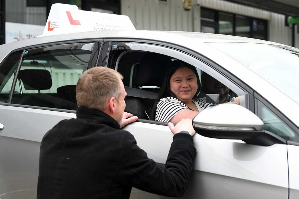 A young woman sat in a car receiving instructions from a Herts Ability assessor.